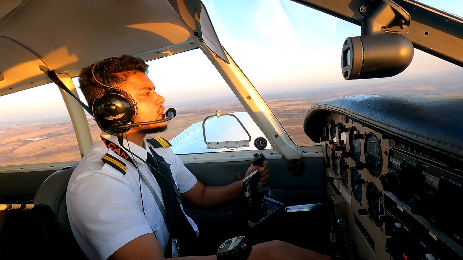 Adam Harry actively flying in a cockpit, wearing a pilot headset with the landscape visible outside